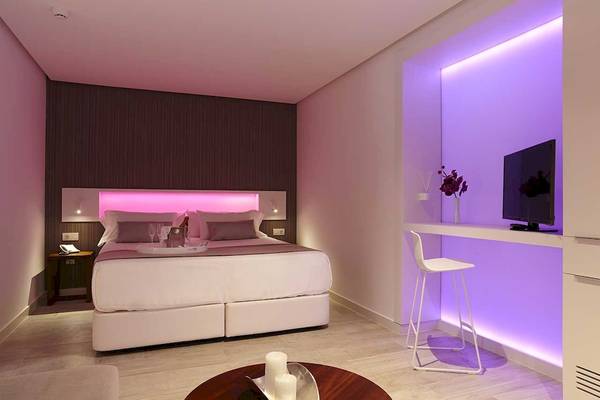 Schlafzimmer mit Bett, Tisch und pinkem Licht im Sentido Garbi Ibiza & Spa Hotel