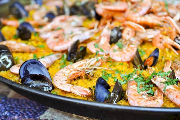 Eine große Platte Paella mit Garnelen und Muscheln, serviert auf einem runden Tisch.