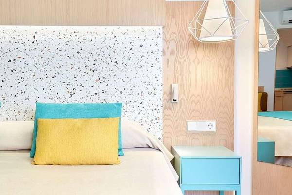 Schlafzimmer im Universal Aparthotel Elisa mit Kopfteil, Kissen, Nachttisch und Lampe.