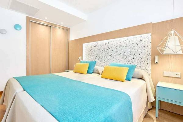 Schlafzimmer im Universal Aparthotel Elisa mit zwei Betten und blauen und gelben Kissen.