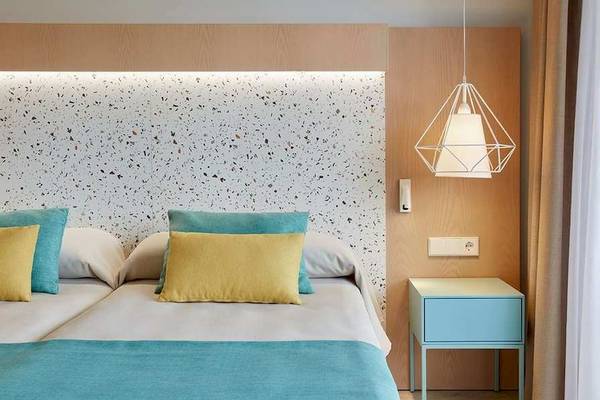 Doppelbett-Zimmer im Universal Aparthotel Elisa mit modernem Design, blauen und gelben Kissen, und einem blauen Nachttisch.
