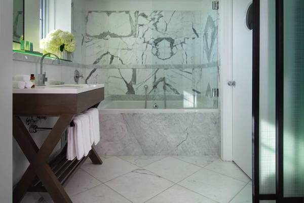 Badezimmer im Victor South Beach Hotel mit Marmorwänden, Badewanne und modernem Waschtisch.
