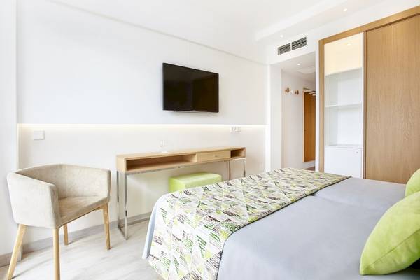 Innenansicht eines Gästezimmers im Castell Royal Hotel mit einem Bett, einem Schreibtisch, einem Fernseher und einem Stuhl.