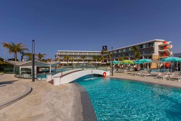 Außenpoolbereich des Faros Hotel Ayia Napa mit Brücke und Sonnenliegen.