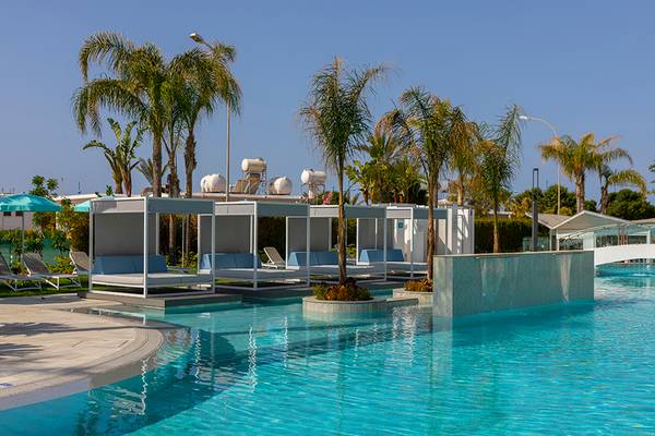 Pool-Lounge-Bereich des Faros Hotel Ayia Napa mit weißen Sonnenliegen und Palmen.