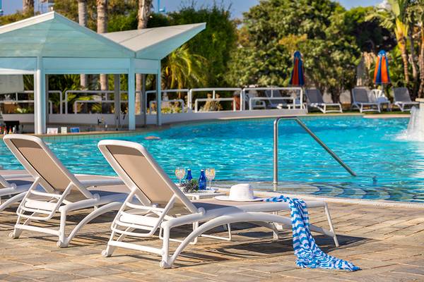 Poolbereich des Faros Hotels Ayia Napa mit weißen Liegestühlen und einer Sonnenmütze
