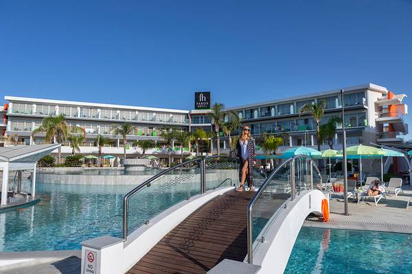 Eine Frau in Sonnenbrille steht auf einer Brücke über dem Swimmingpool im Faros Hotel Ayia Napa.