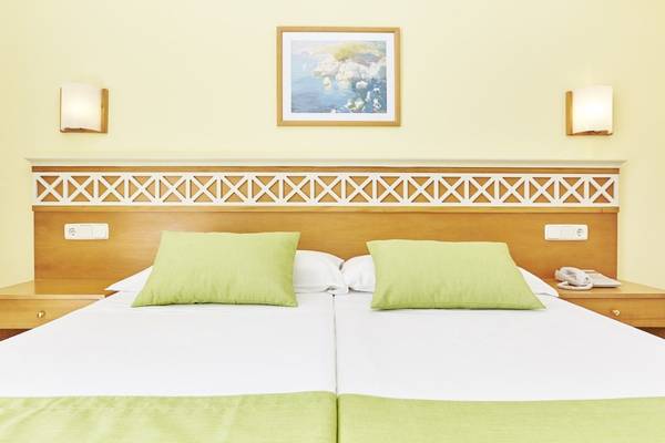 Doppelbett im Hotelzimmer des Bikini Hotels mit grünen Kissen und gelber Wand.