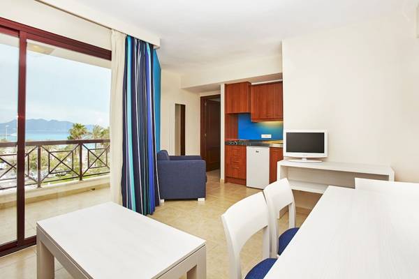 Innenansicht eines Zimmers im Bikini Hotel mit Meerblick, einem Schreibtisch, einem Fernseher, einem Sessel und einer Küchenzeile.