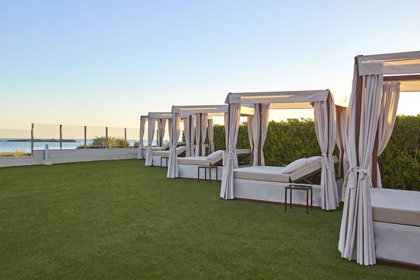 Reihe von weißen Liegebetten mit Vorhängen auf einer Terrasse mit Blick auf das Meer.