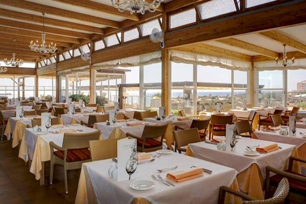 Innenansicht des Restaurants im Grand Leon & Spa Hotel mit vielen Tischen, Stühlen und einer Aussicht auf das Meer.