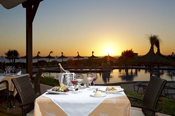 Ein Tisch mit Essen und Wein vor dem Grand Leon & Spa Hotel am Pool bei Sonnenuntergang.