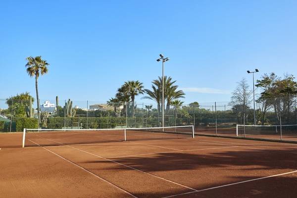 Tennisplatz im Grand Leon & Spa Hotel mit blauem Himmel und Palmen im Hintergrund.