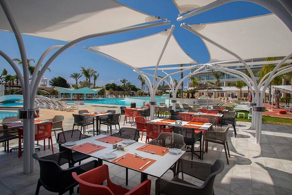 Restaurantterrasse des Faros Hotel Ayia Napa mit Tischen und Stühlen unter weißen Sonnensegeln.