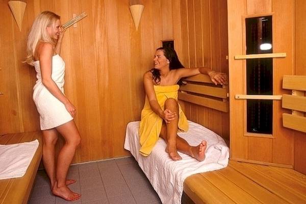 Zwei Frauen in einer Sauna im Grand Leon & Spa Hotel, eine sitzt auf einem Bett, die andere steht und lächelt.