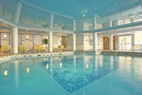Innenansicht des Schwimmbeckens im Grand Leon & Spa Hotel mit gelben Sonnenliegen und blauer Decke.
