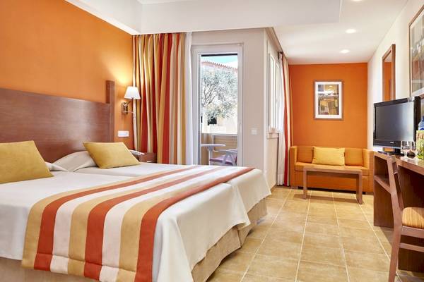 Innenansicht eines Doppelzimmers im Grand Leon & Spa Hotel mit zwei Betten, Couch, Fernseher und Balkon.