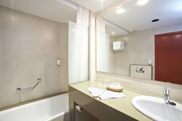 Badezimmer im Grand Leon & Spa Hotel mit Badewanne, Spiegel, Waschbecken und Handtüchern.