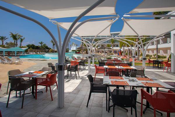 Außenbereich des Restaurants im Faros Hotel Ayia Napa mit Tischen und Stühlen unter Sonnenschirmen.