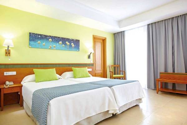 Doppelbettzimmer im Laguna Hotel mit gelben Wänden, grünen Kissen und einer blauen Wanddekoration.