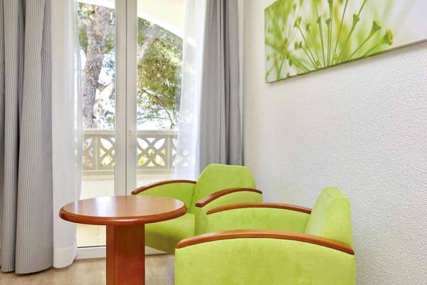 Zimmer im Laguna Hotel mit grünen Sofas und einem runden Tisch vor einem Balkon.