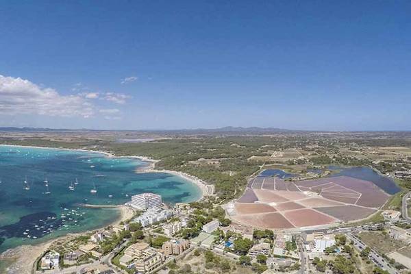 Luftaufnahme von Salinas in Ibiza mit Hotel im Hintergrund, Salzfeldern und einer Bucht mit Booten.