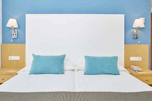 Doppelbett im Zimmer des Marques Hotels mit blauen Kissen und weißen Laken.