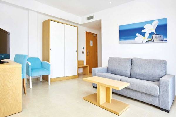 Innenansicht eines Zimmers im Marques Hotel mit einem Sofa, zwei Stühlen, einem Tisch, einem Fernseher und einem Gemälde.