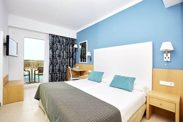 Zimmer im Marques Hotel mit Balkon und Meerblick, zeigt ein Doppelbett mit blauen Kissen und blauen Wänden.