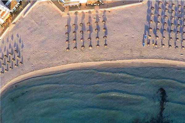 Luftaufnahme der Perla Hotel Strand mit vielen Sonnenschirmen und Gästen am Meer