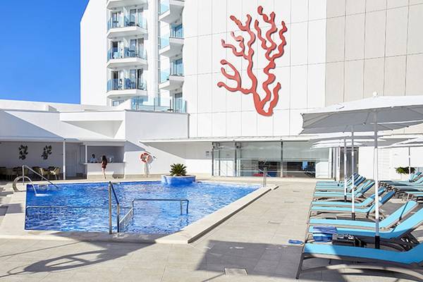 Außenpoolbereich des Perla Hotels mit Loungestühlen und rotem Korallendesign an der Wand.