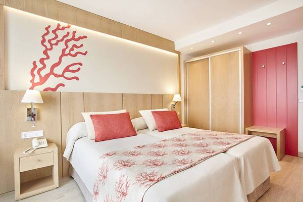 Doppelbettzimmer im Perla Hotel mit rotem Korallen-Design und modernem Interieur.