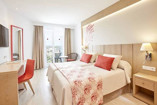 Innenansicht eines Doppelzimmers im Perla Hotel mit zwei Betten, Schreibtisch, Stühlen und einem Ausblick auf die Stadt.