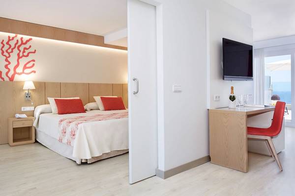 Innenansicht eines Zimmers im Perla Hotel mit Bett, Schreibtisch und Fernseher.