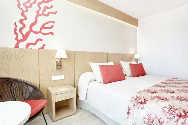 Hotelzimmer im Perla Hotel mit weißem Bett, roten Kissen, rotem Wandmuster und Nachttisch.