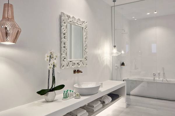 Ein modernes Badezimmer in den Katikies Villas Mykonos mit weißen Wänden, einem Badezimmerspiegel und einer Badewanne.