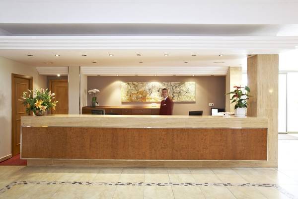 Empfangsbereich des Romantica Hotels mit Rezeptionstresen, Blumen, und Angestelltem.