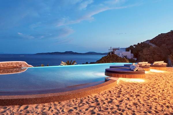 Katikies Villas Mykonos Pool bei Nacht mit Blick auf das Meer und eine Villa im Hintergrund.