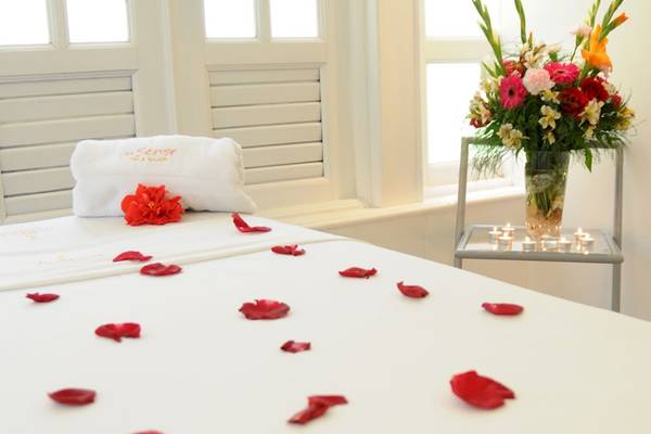 Ein Bett im Coral Costa Caribe Beach Resort, geschmückt mit roten Rosenblättern, einem weißen Handtuch und einer Blumenvase.
