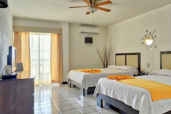 Doppelzimmer im Coral Costa Caribe Beach Resort mit zwei Betten, Klimaanlage, Fernseher und Fenster mit gelben Vorhängen.