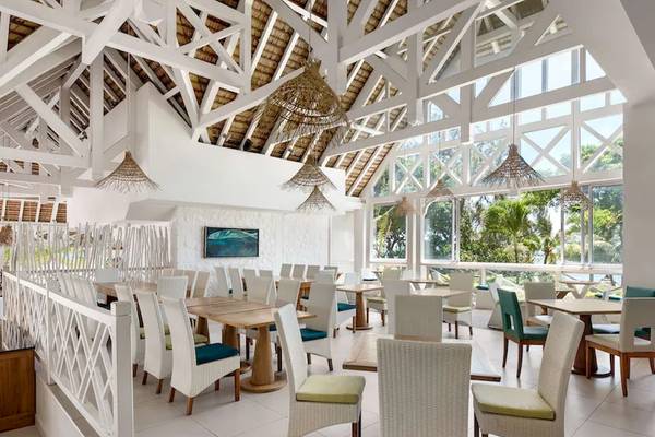Innenansicht des Restaurants im Radisson Blu Azuri Resort & Spa mit weißen Tischen und Stühlen, hellen Wänden und Deckenlampen.