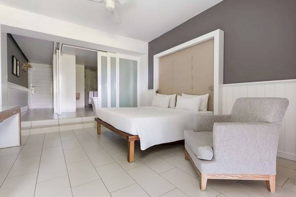 Innenansicht eines Schlafzimmers im Radisson Blu Azuri Resort mit einem Bett, einer Chaiselongue und einer Glastür.