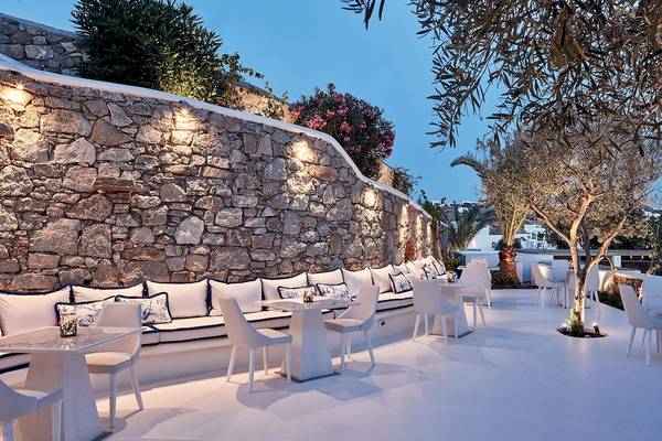 Terrasse des Katikies Villas Mykonos mit Steinwand, Möbeln und beleuchteten Bäumen