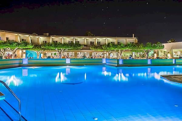 Nachtansicht des Swimmingpools des Sandy Beach Hotels auf Kos mit beleuchteten Gebäuden und Bäumen