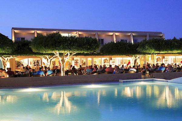 Abendliche Pool-Lounge im Sandy Beach Hotel auf Kos mit Gästen, die sich unter Bäumen versammelt haben.