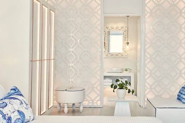 Innendesign eines Zimmers im Katikies Villas Mykonos mit weißen Wänden, geometrischen Mustern, einem weißen Couch, einem weißen Tisch mit einer Pflanze und einem weißen Waschbecken.
