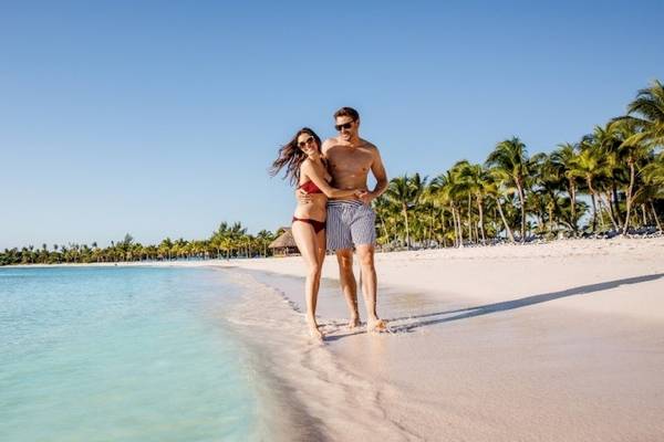 Ein Paar am Strand von Barcelo Maya Beach, umgeben von Palmen und klarem Wasser.