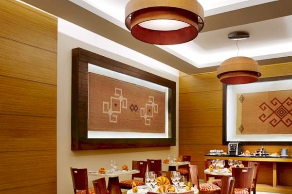 Innenbereich des Barcelo Maya Beach Hotels mit gerahmten Wanddekorationen, runden Kronleuchtern, Holzmöbeln und einer Bar.