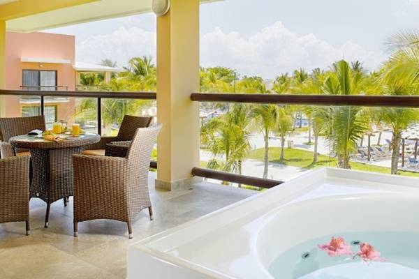 Balkon des Barcelo Maya Beach Hotel mit Blick auf einen Whirlpool und einen Tisch mit Sonnenschirmen.
