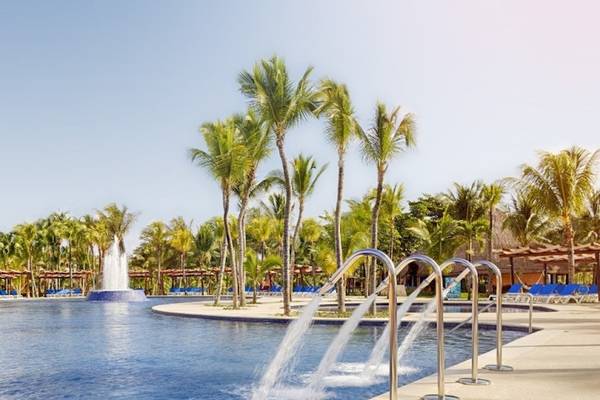 Ein Swimmingpool im Barcelo Maya Beach Hotel mit Palmen und Liegestühlen.